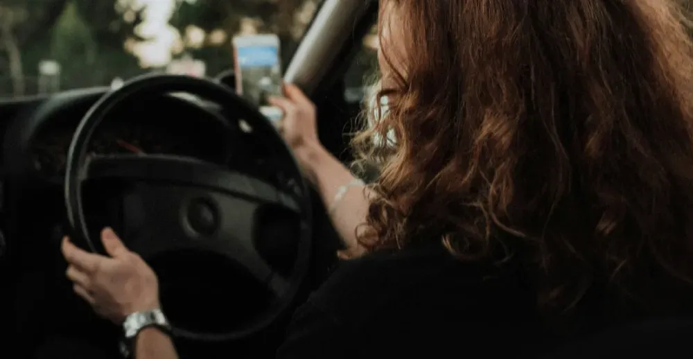 A woman is driving a car and looking at her phone.
