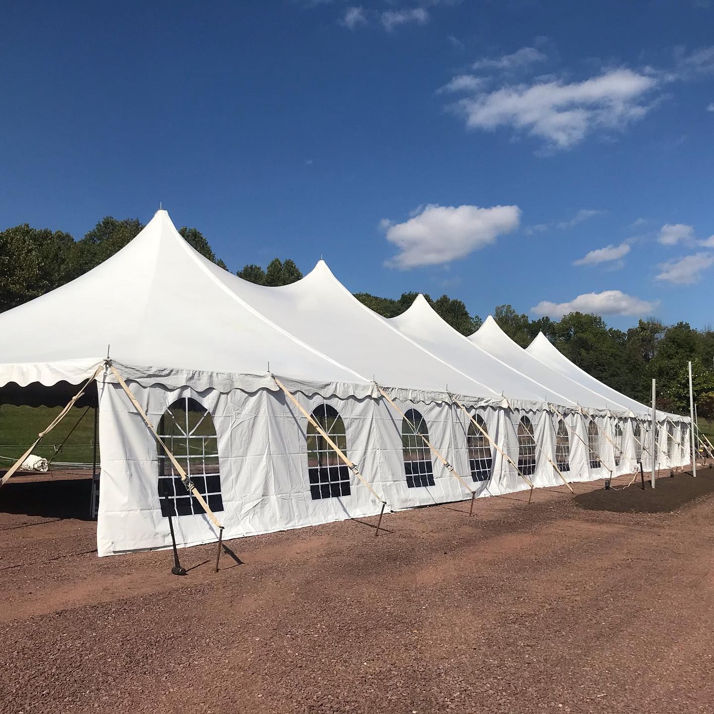 White event tent with arched windows on a gravel area, under a blue sky with clouds.