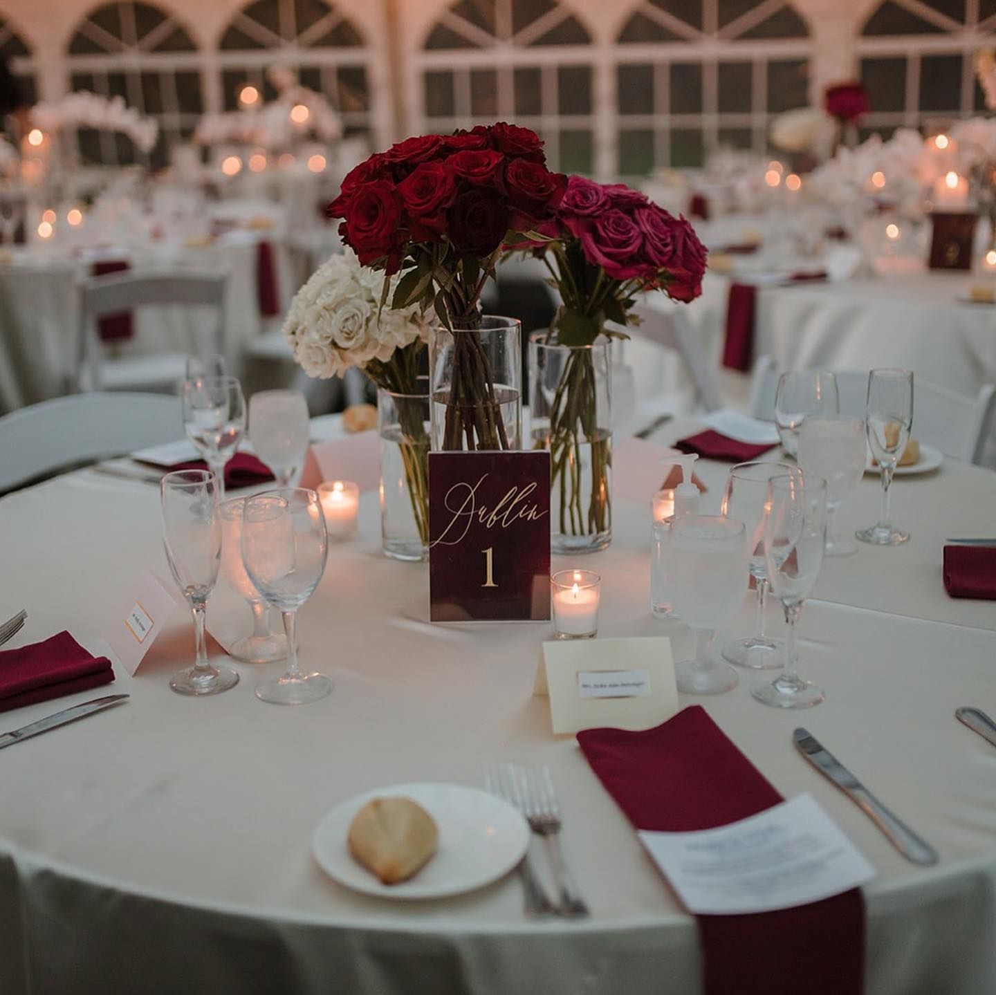 Elegant wedding reception table set with flowers, candles, and burgundy accents.