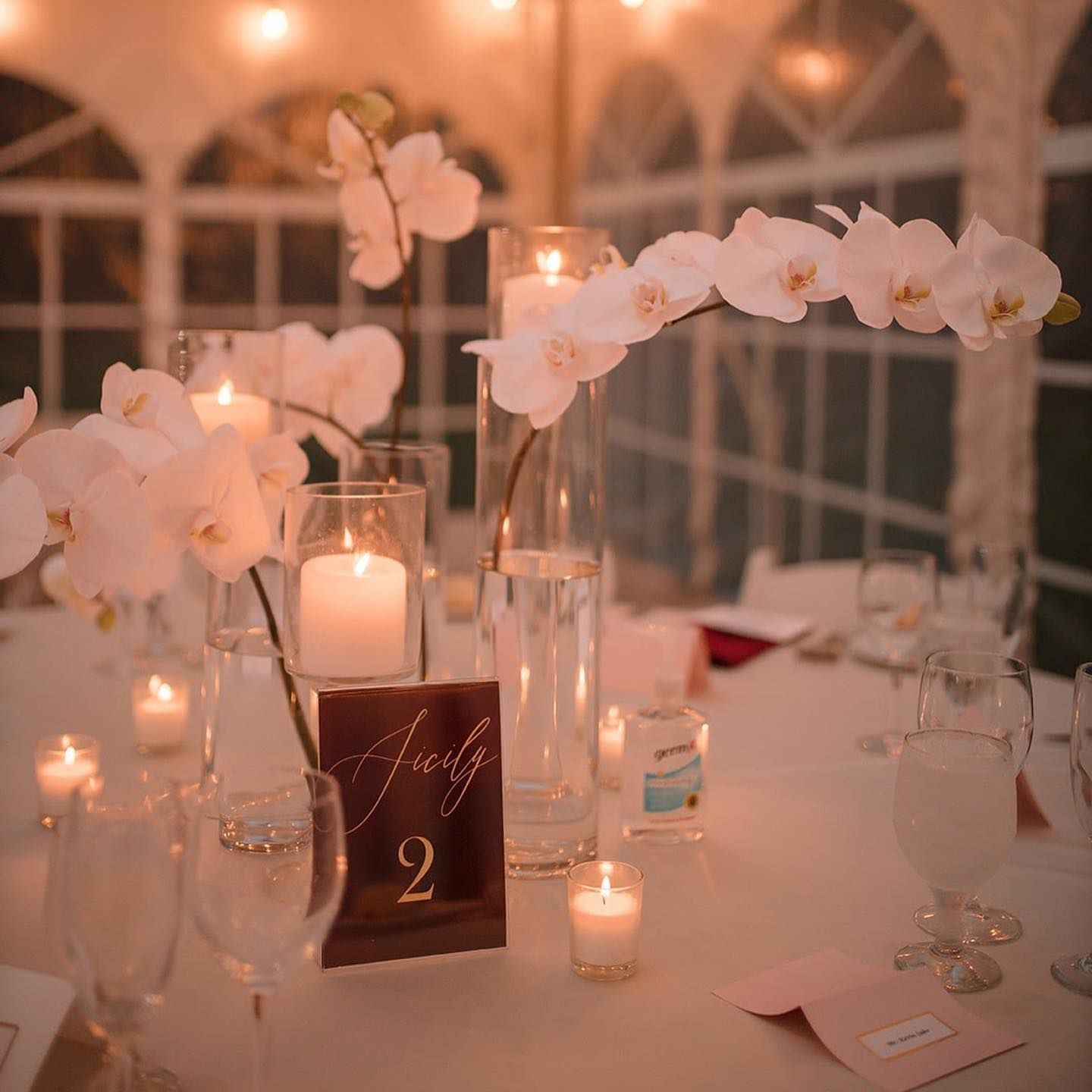 Elegant table setting with orchid centerpieces, candles, and a table number card.