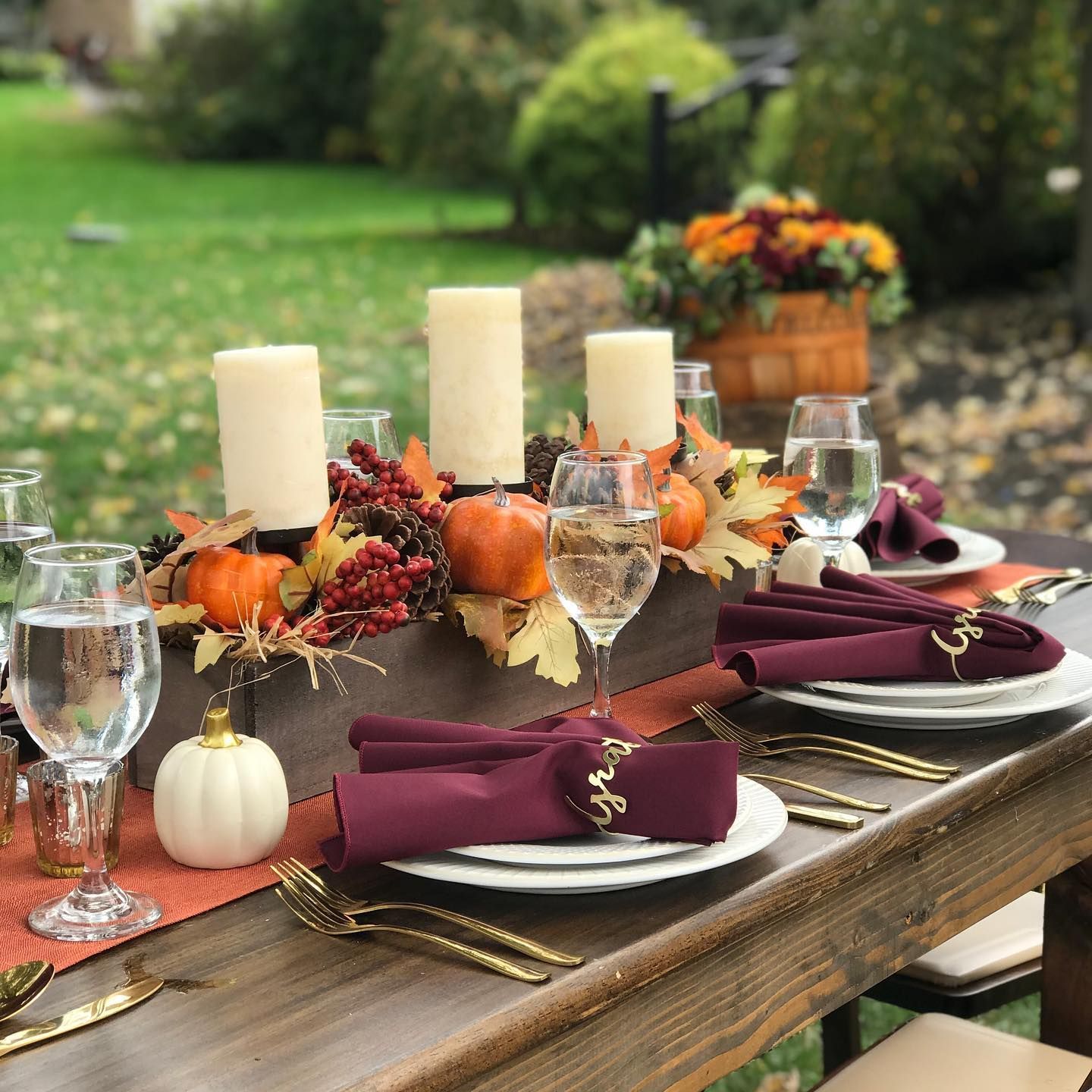 Outdoor table set for fall with candles, pumpkins, and burgundy napkins.