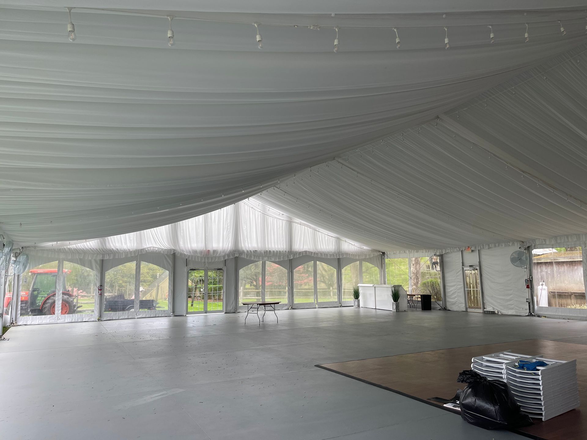 Interior of a large white tent with open windows overlooking a grassy area. Grey floor, overhead white draping.