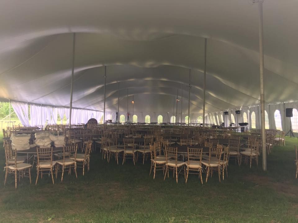 Rows of gold chairs set up inside a large white tent on a grassy lawn, ready for an event.