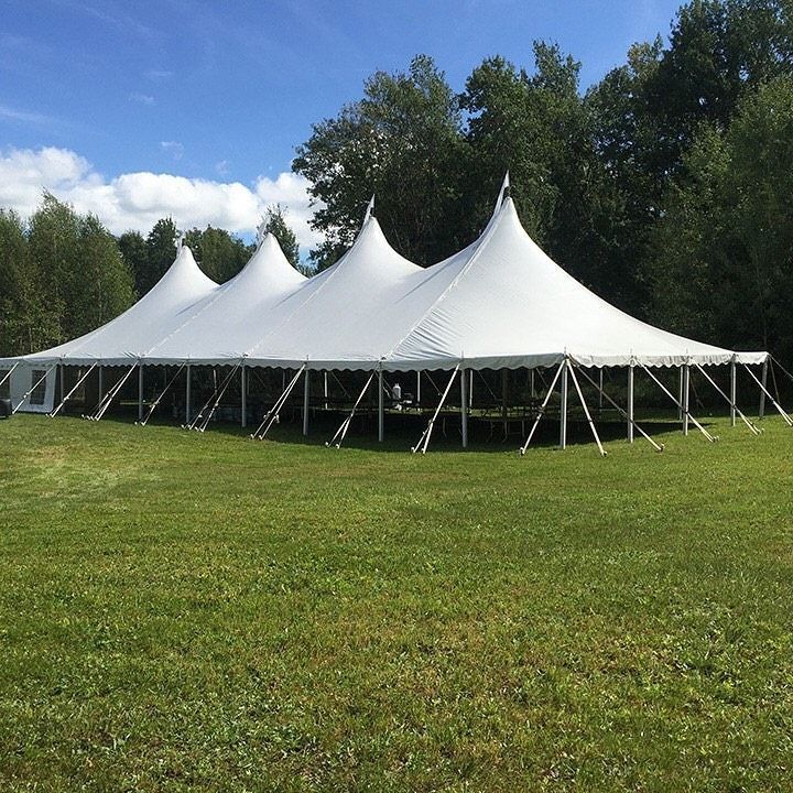 White event tent on a grassy field with trees in the background under a blue sky.