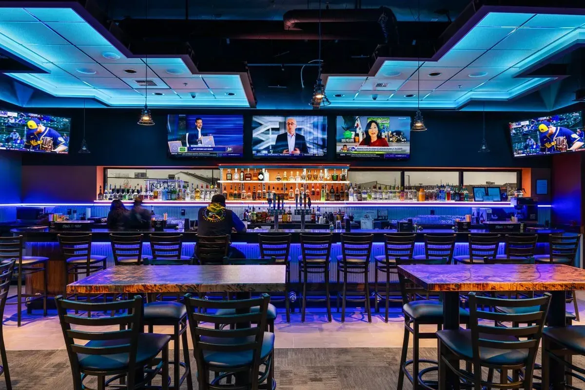 A restaurant with tables and chairs and a bar with blue lights.