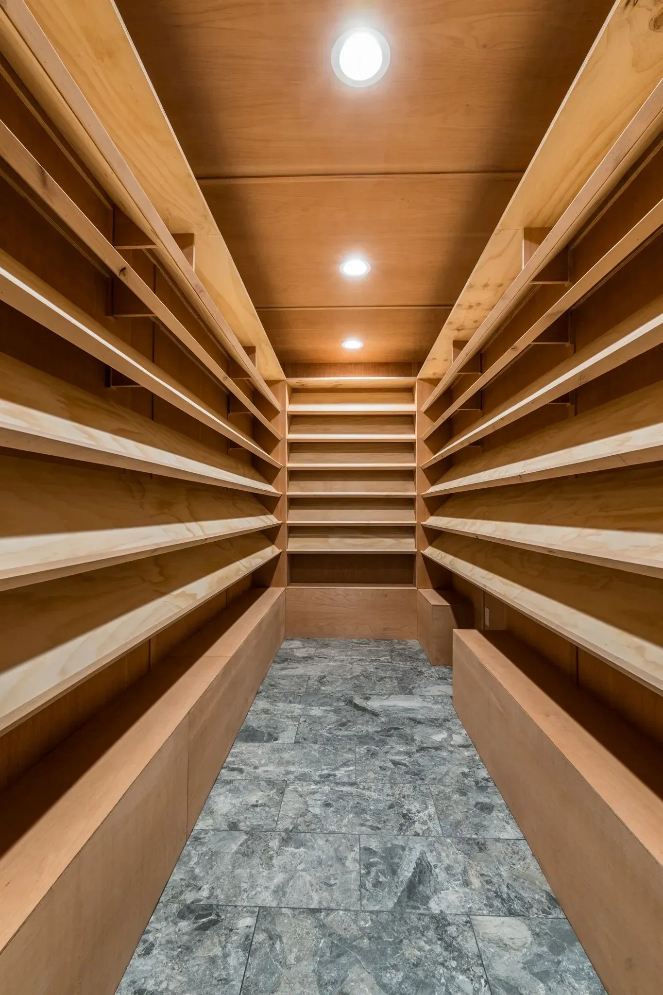 An empty walk in closet with wooden shelves and a marble floor.