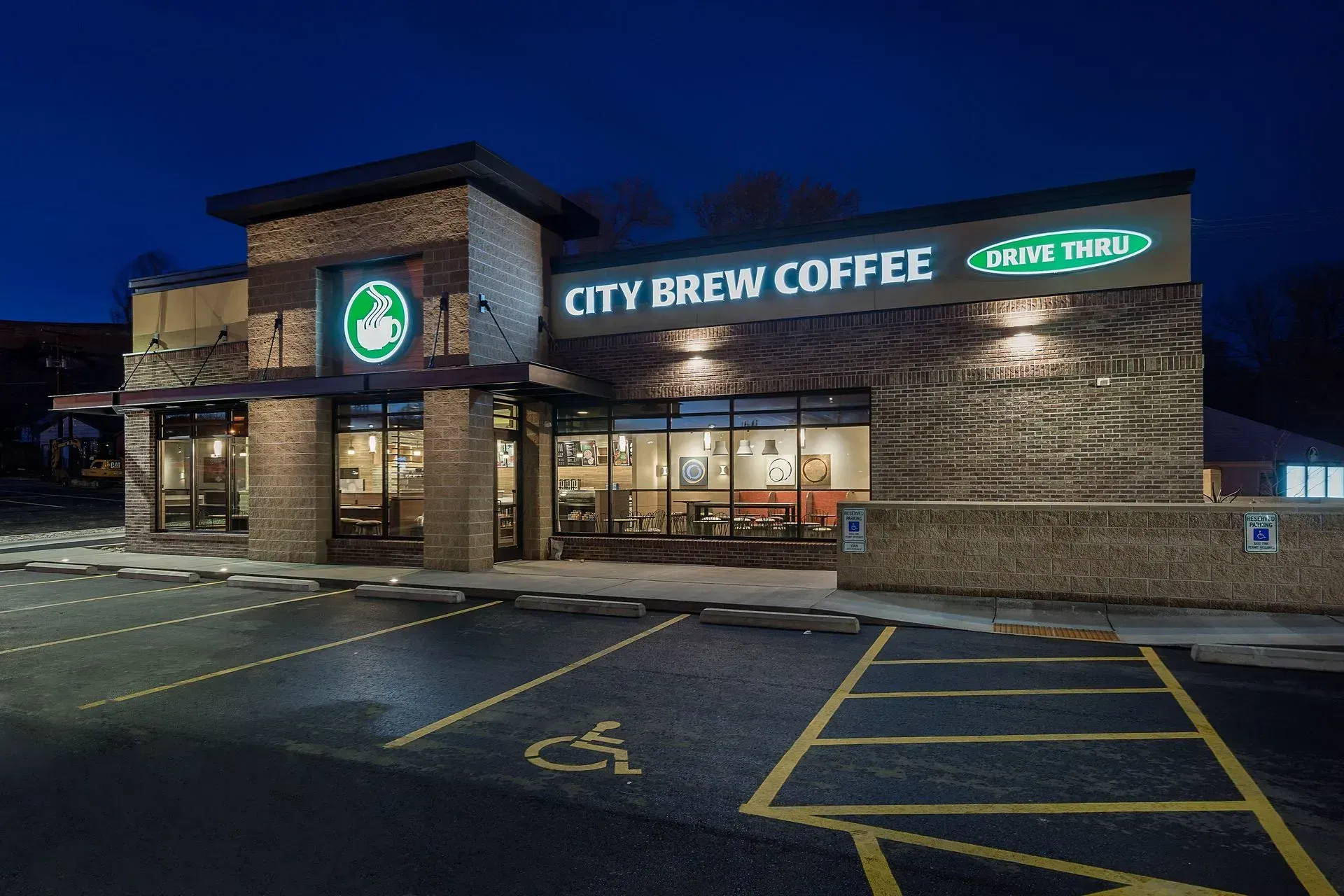 A city brew coffee shop is lit up at night with a handicapped parking spot in front of it.