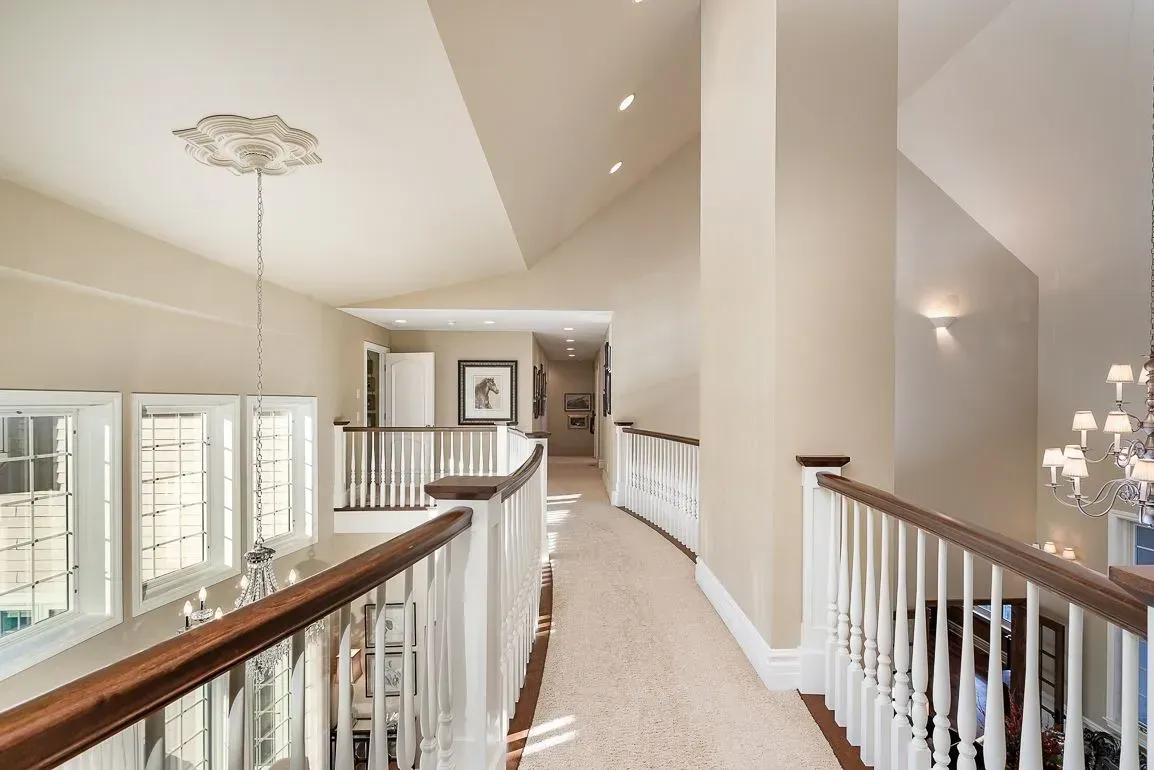 A hallway with a railing and a chandelier in a house.