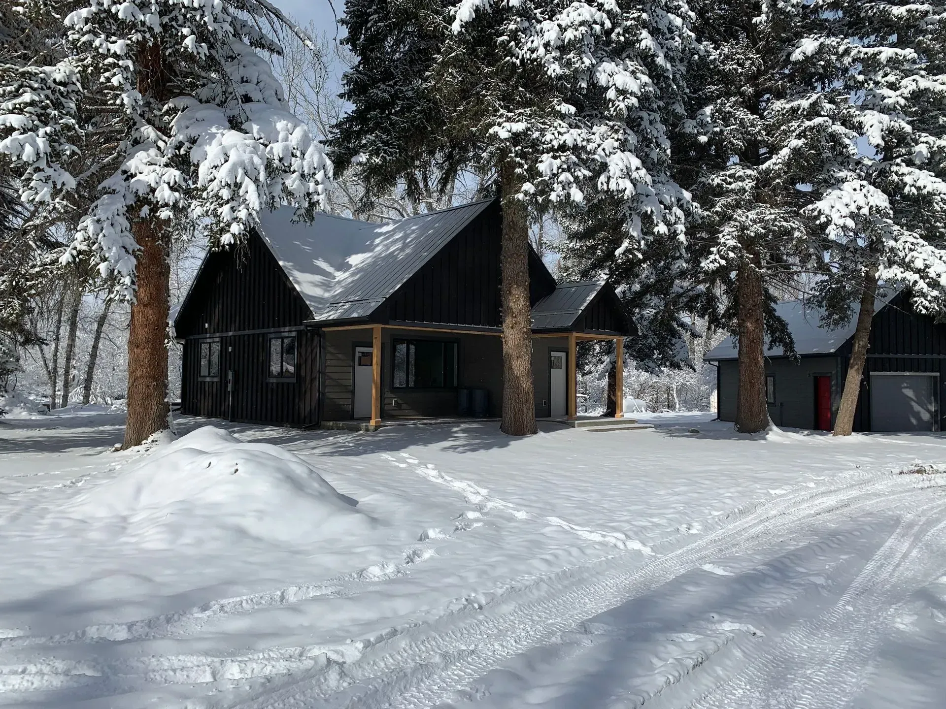 A couple of cabins covered in snow with trees in the background.
