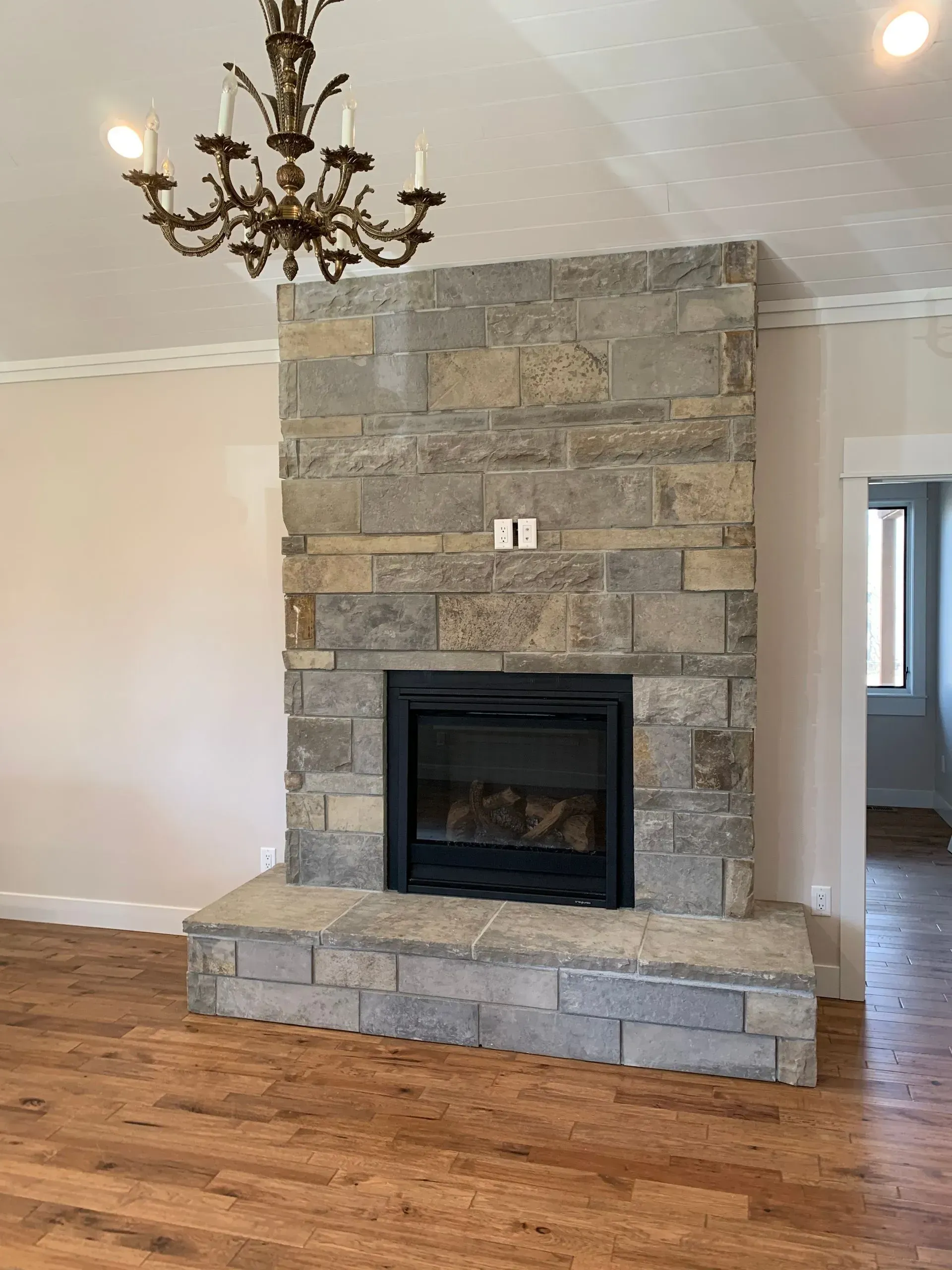 A living room with a stone fireplace and a chandelier hanging from the ceiling.