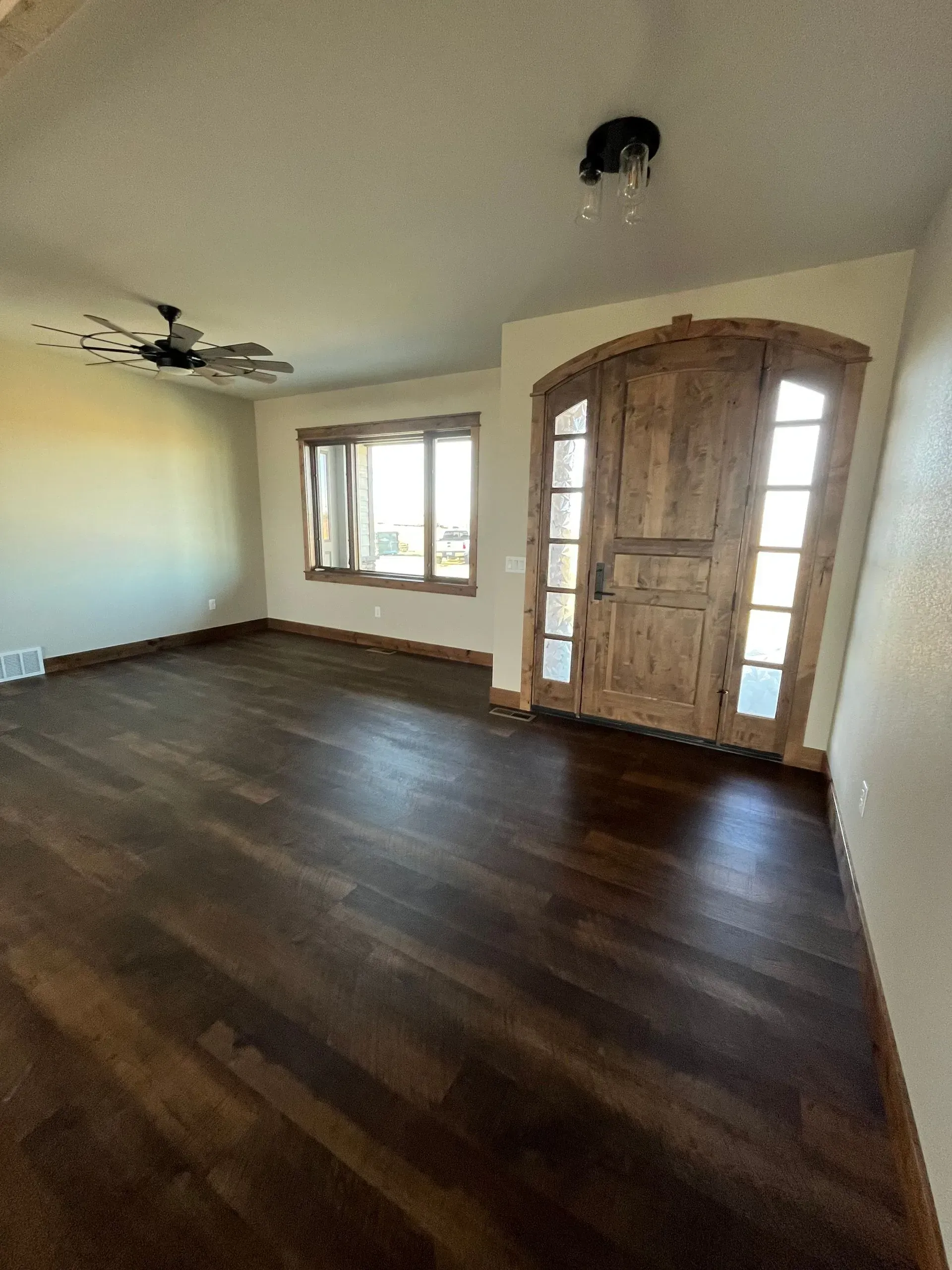 An empty living room with hardwood floors and a ceiling fan.