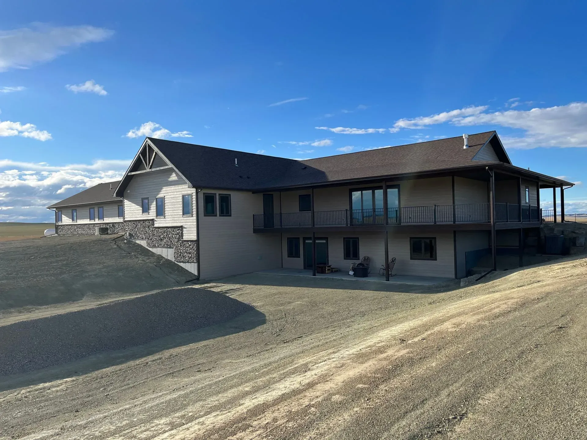 A large house is sitting on top of a dirt hill in the middle of a field.
