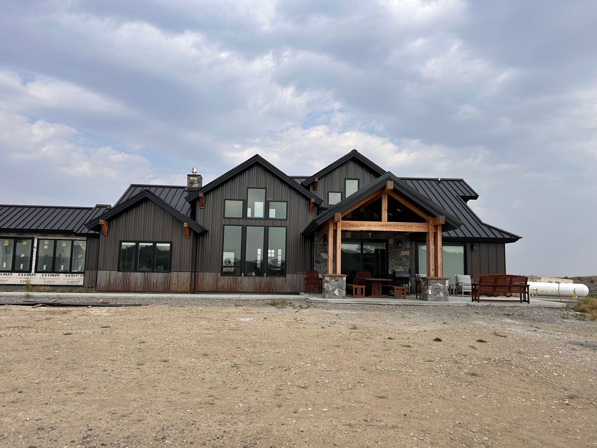 Dark wood cabin with covered porch and stone accents under cloudy sky.