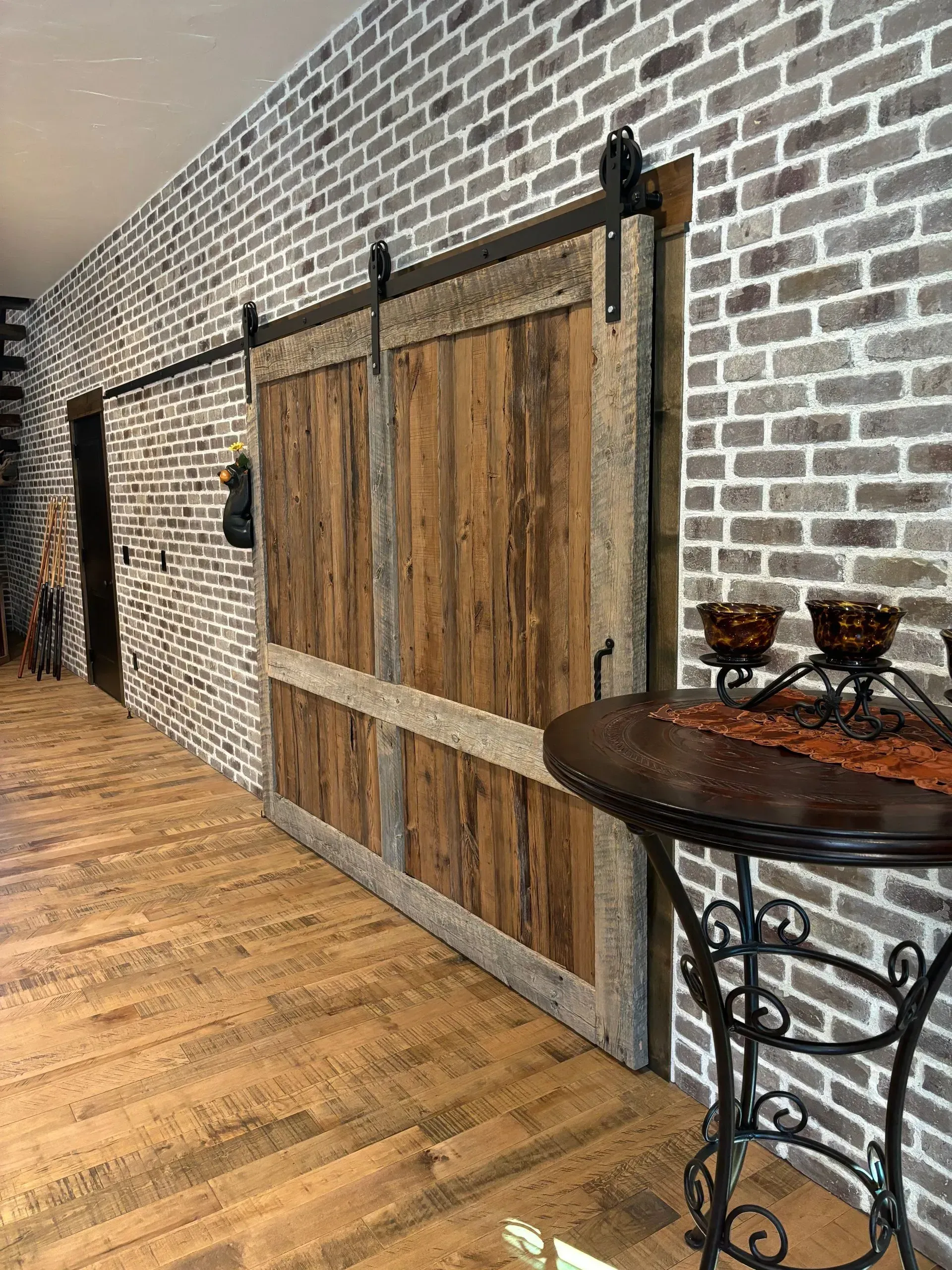 A wooden sliding barn door is hanging on a brick wall next to a table.