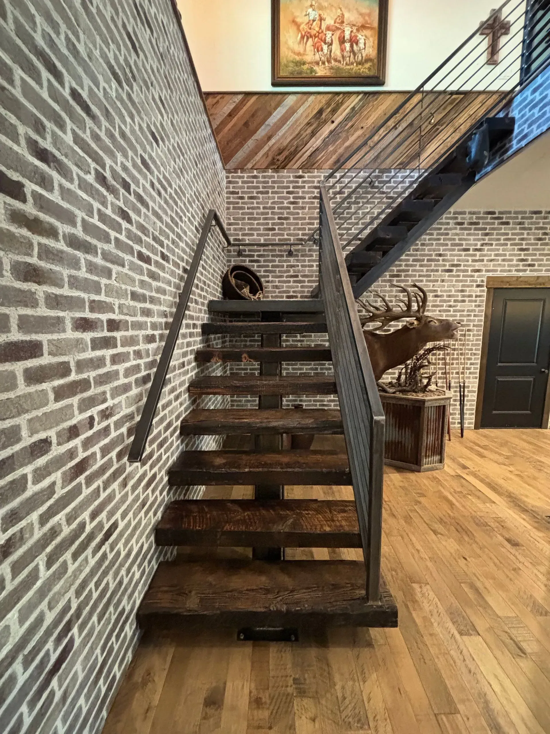 A wooden staircase with a metal railing in a room with a brick wall.