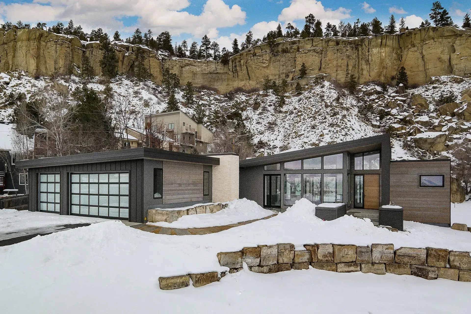 A modern house is sitting on top of a snow covered hill.
