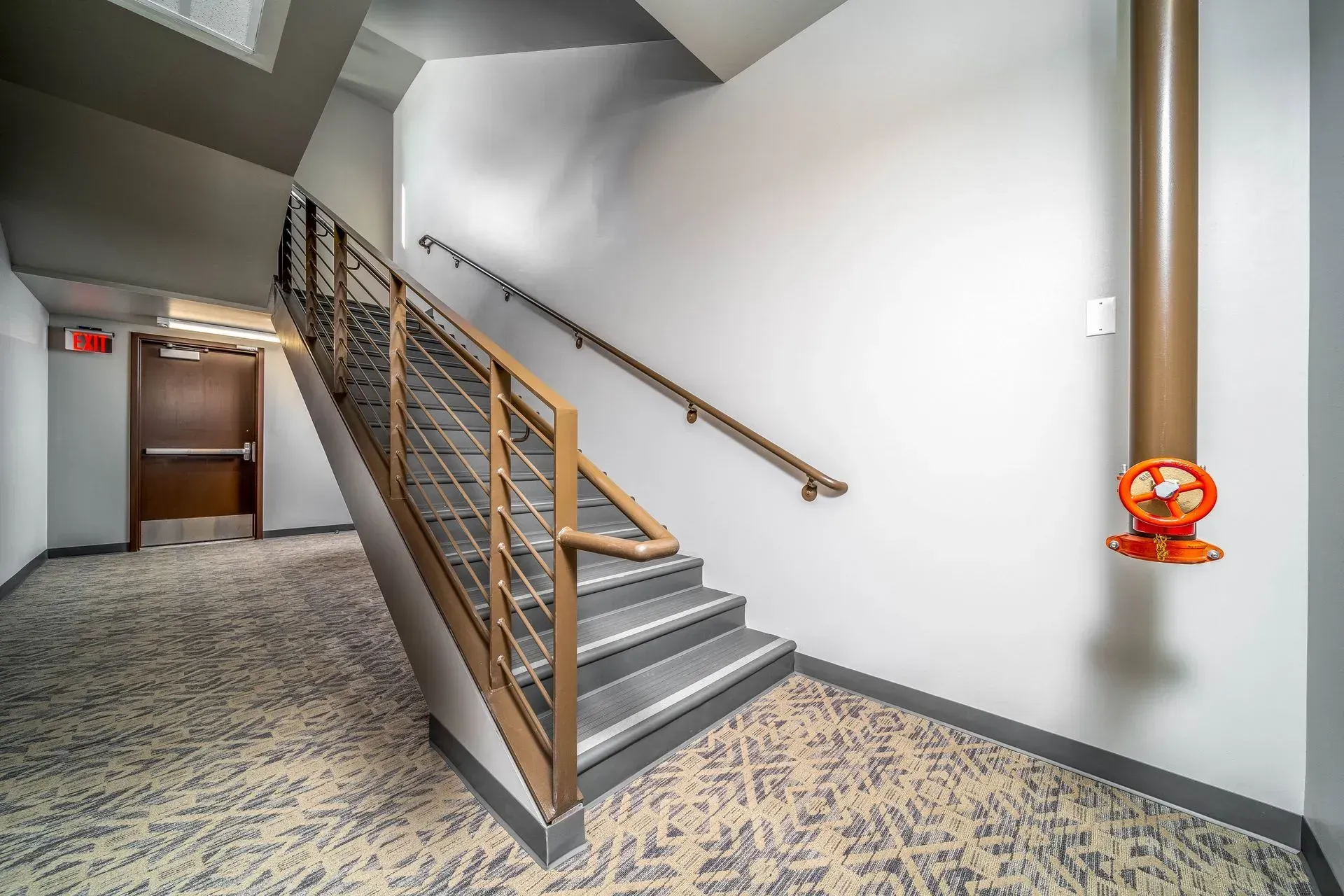 A hallway with stairs and a fire hydrant on the wall.