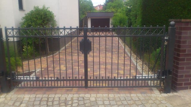 Ein schwarzes schmiedeeisernes Tor öffnet sich zu einer Auffahrt, die zu einem Haus führt.