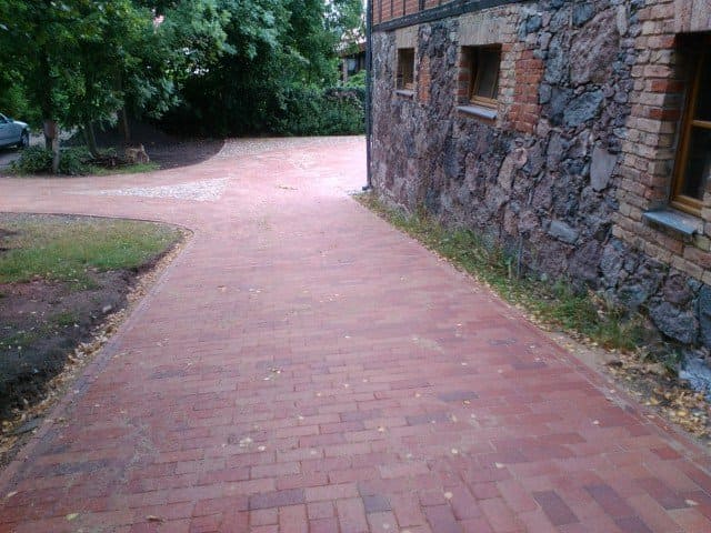Ein roter Backsteinweg führt zu einem Steingebäude.
