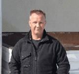 Ein Mann in einer schwarzen Jacke steht vor einem Gebäude.