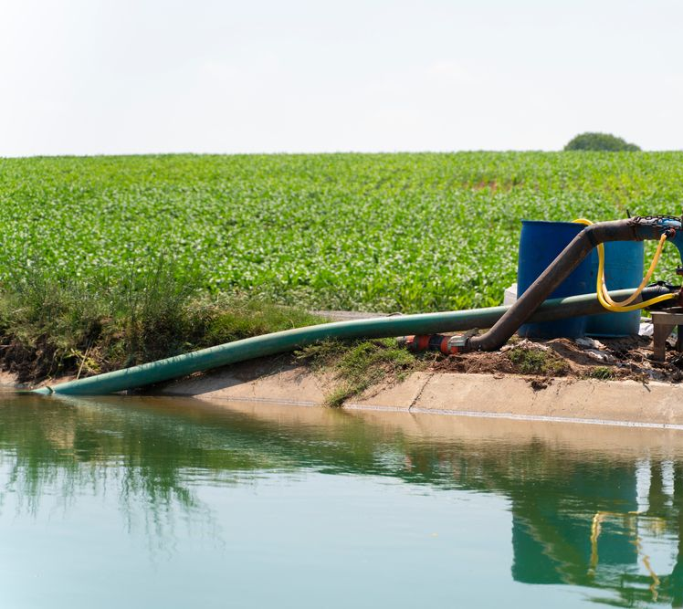 Water Pump With Green Hose in a Canal — Paap's Cleansing Services in Branyan, QLD