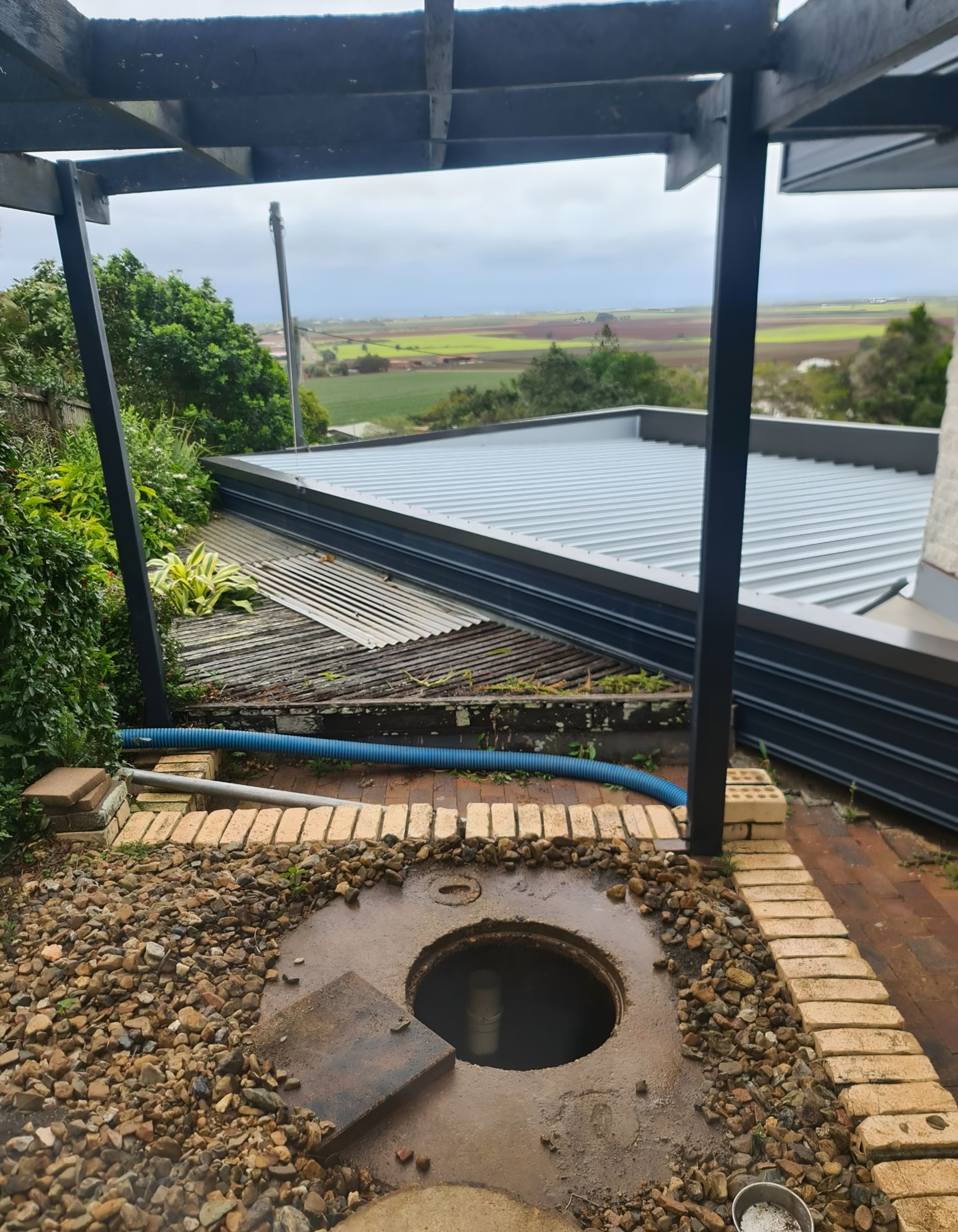 Open Manhole in a Brick-lined Area Under a Slatted Pergola — Paap's Cleansing Services in Lowmead, QLD