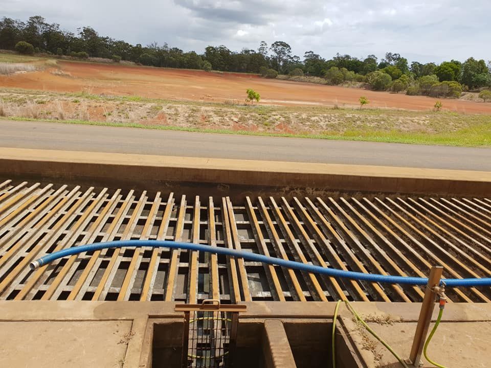 Steel Grate Over a Water Channel With a Blue Hose — Paap's Cleansing Services in Branyan, QLD