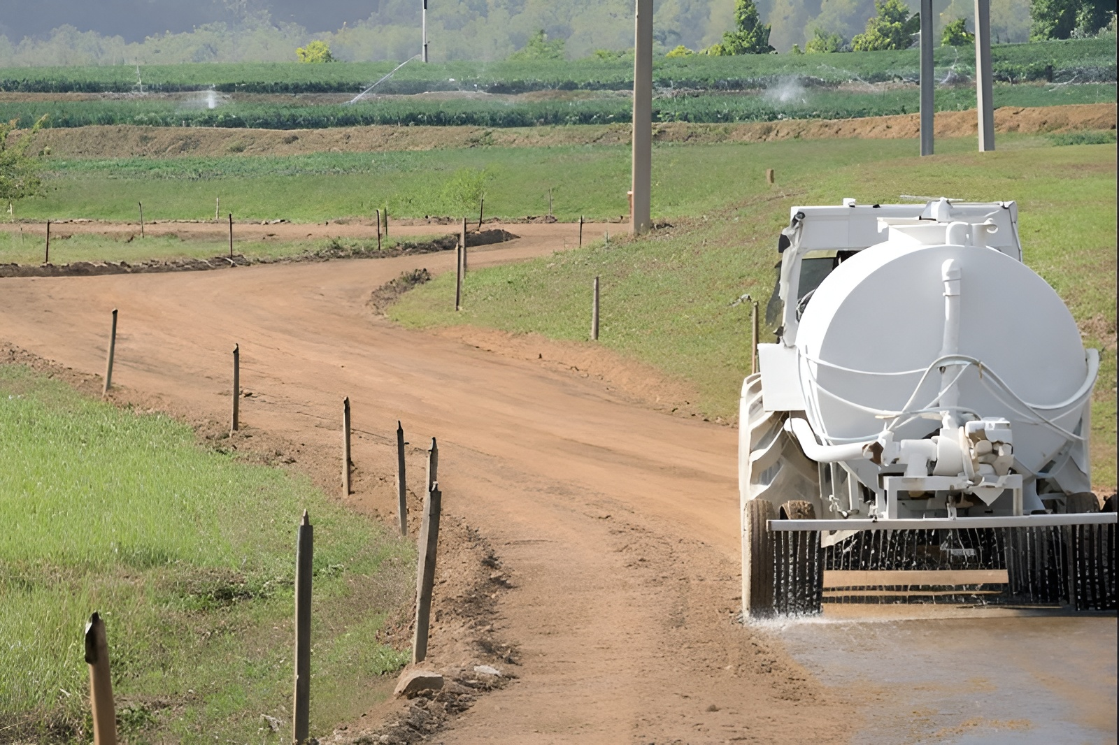 Tractor Spraying Water on Dirt Road in Front of Farmland — Paap's Cleansing Services in Branyan, QLD