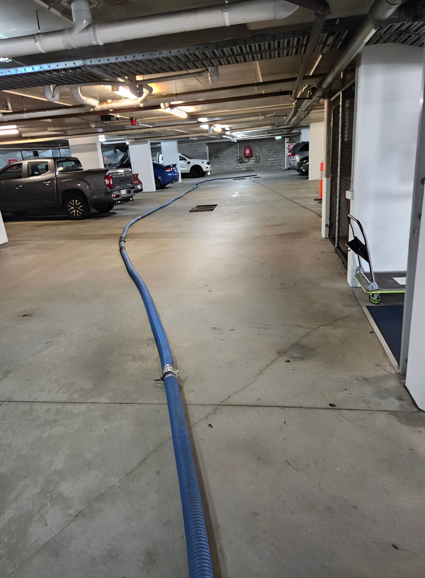 Blue Hose Snaking Across a Concrete Parking Garage Floor — Paap's Cleansing Services in Woodgate, QLD