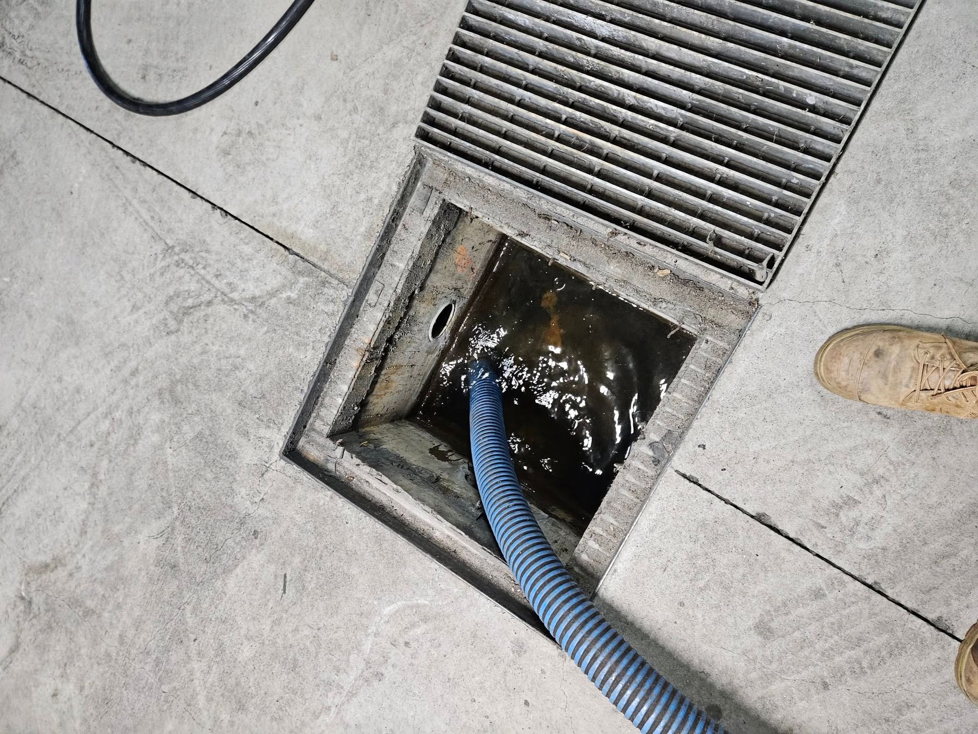 Hose Draining Dark Liquid From a Floor Drain — Paap's Cleansing Services in Lowmead, QLD