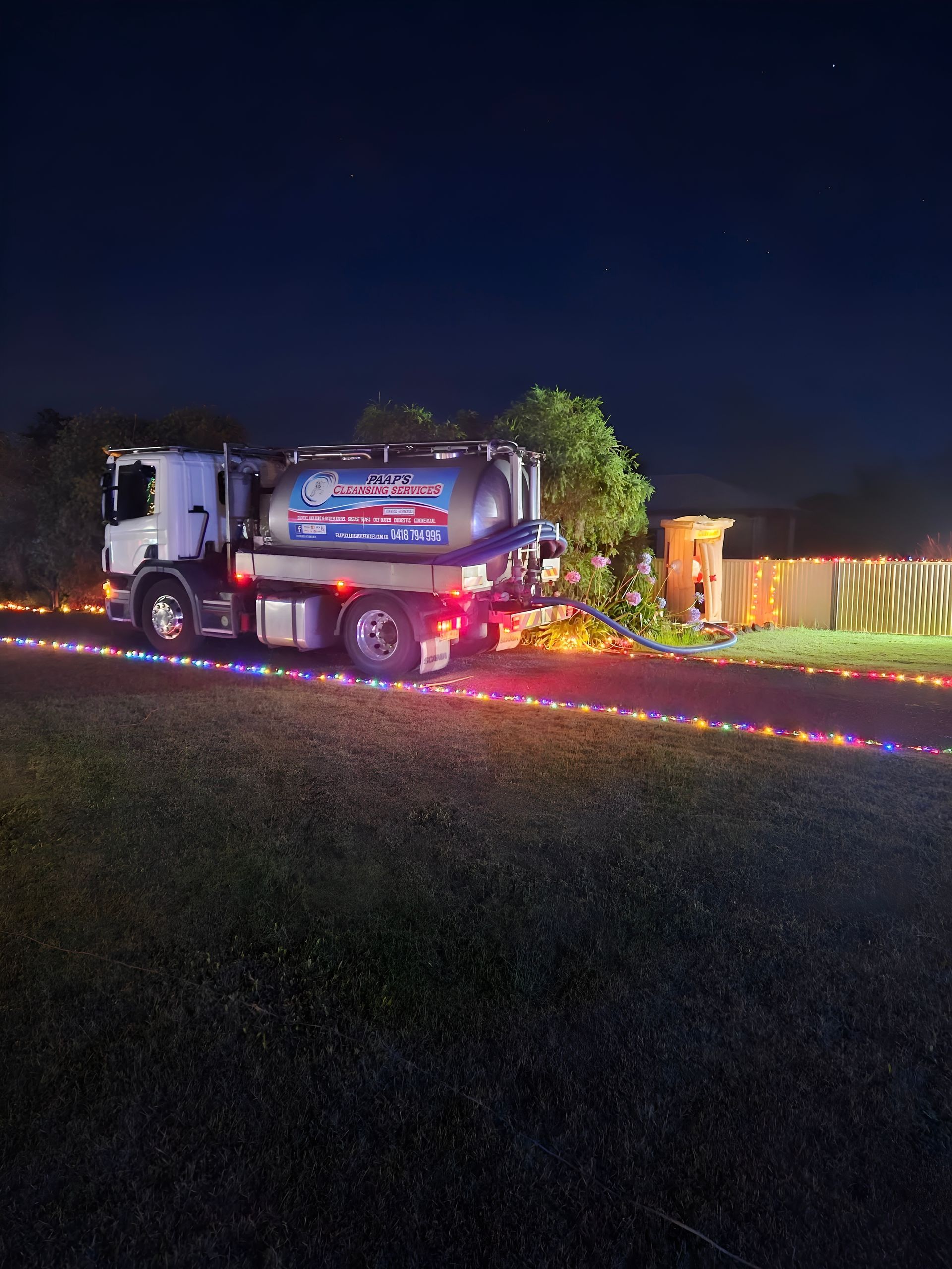 A septic truck parked at night, with a string of colorful lights — Paap's Cleansing Services in Branyan, QLD