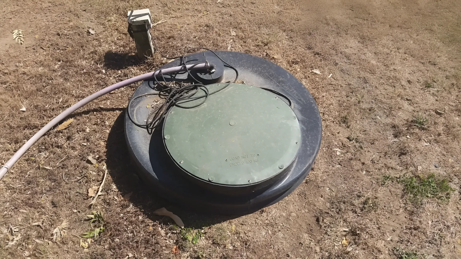 Septic Tank Lid in Dirt With Hose and Small Control Box — Paap's Cleansing Services in Branyan, QLD