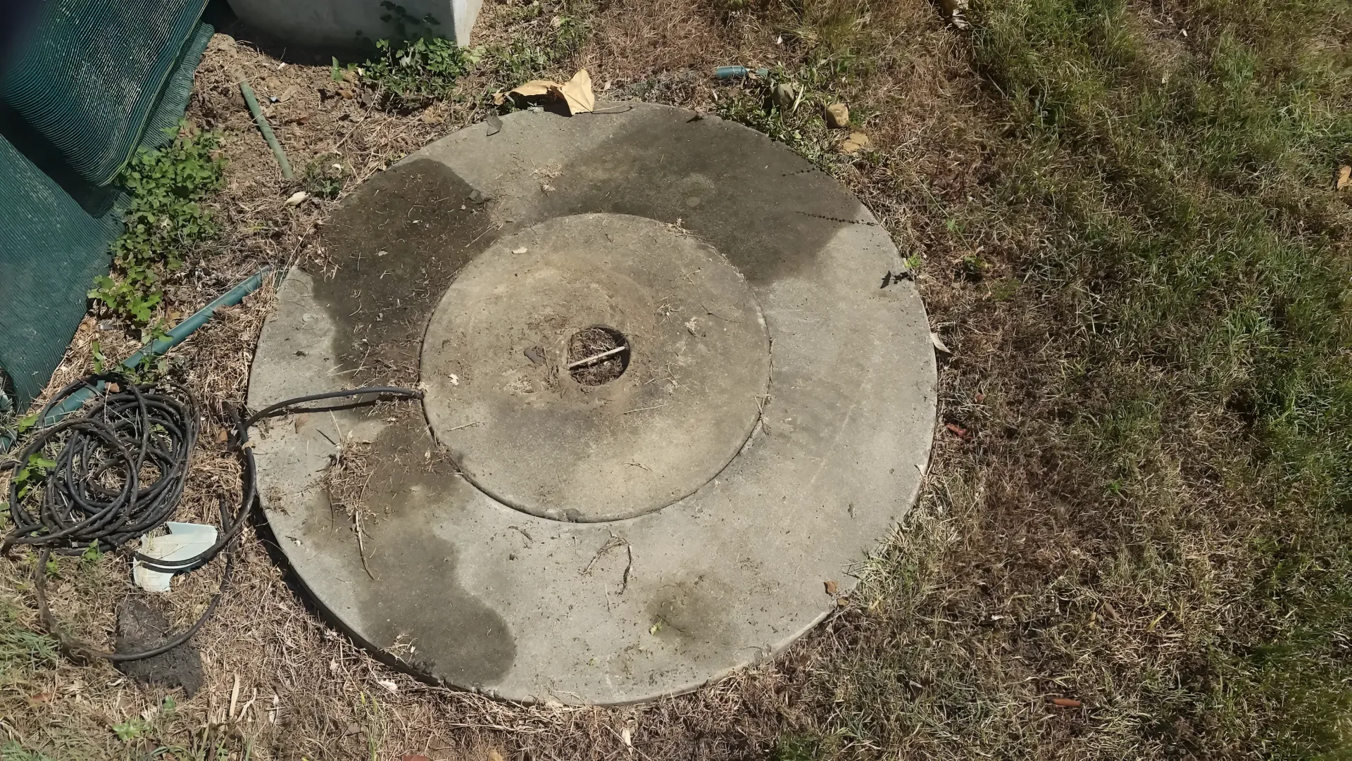 Circular Concrete Well Cover on the Ground, Surrounded by Grass and Dirt — Paap's Cleansing Services in Branyan, QLD