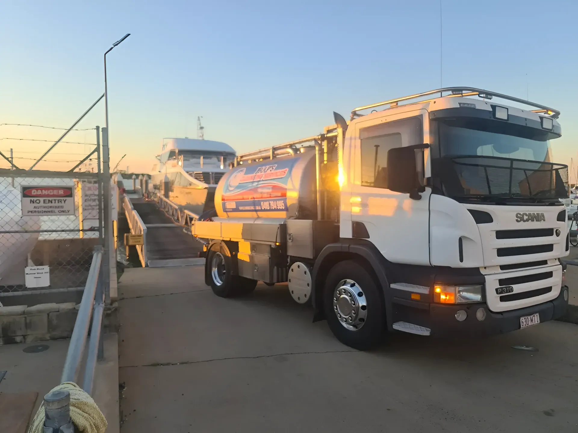 White Tanker Truck Parked on a Pier, Beside a Ferry. — Paap's Cleansing Services in Branyan, QLD
