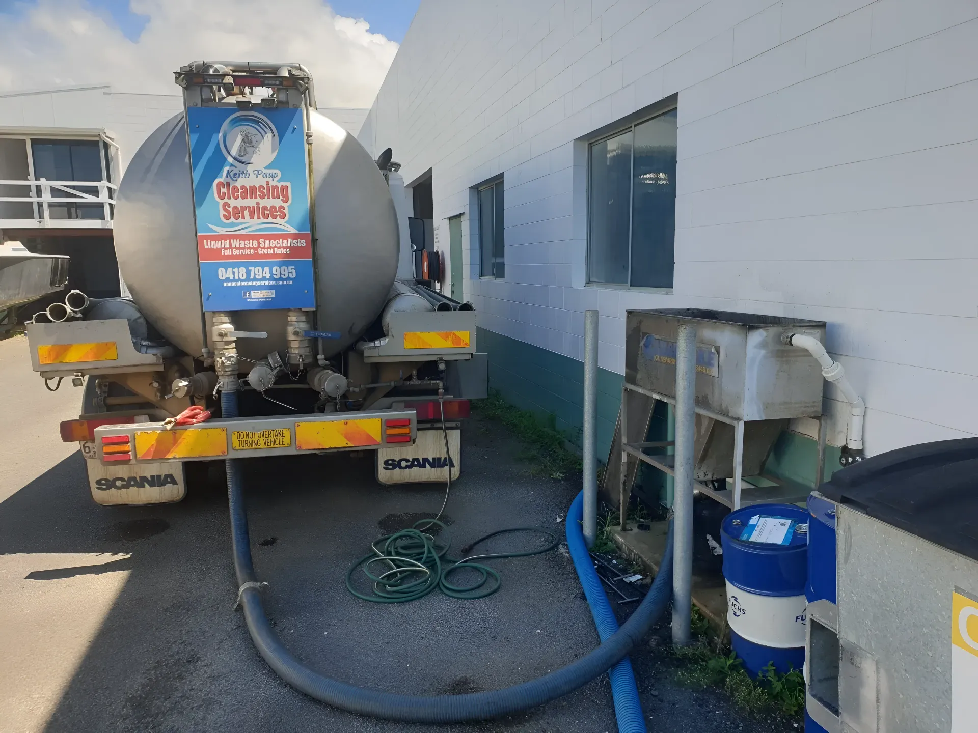 A milk tanker truck unloading at a building, with hoses connected — Paap's Cleansing Services in Branyan, QLD