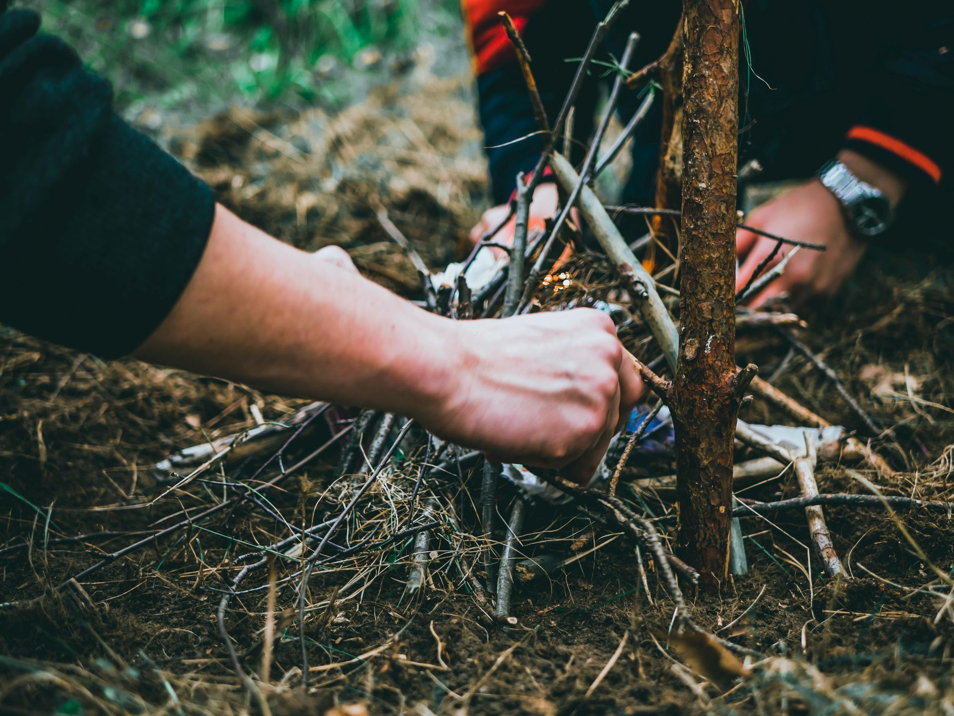 A person is making a fire with sticks in the woods.