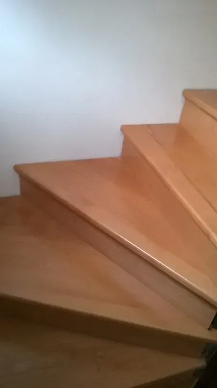 Un primo piano di una scala in legno con un muro bianco sullo sfondo.