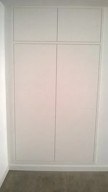 Un armadio bianco è incassato in una parete di una stanza.