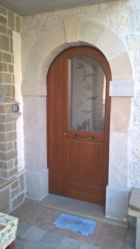 Una porta di legno con una finestra di vetro è circondata da muri di pietra.