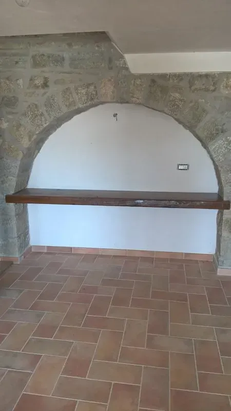 Una stanza vuota con un muro di pietra e un pavimento piastrellato.