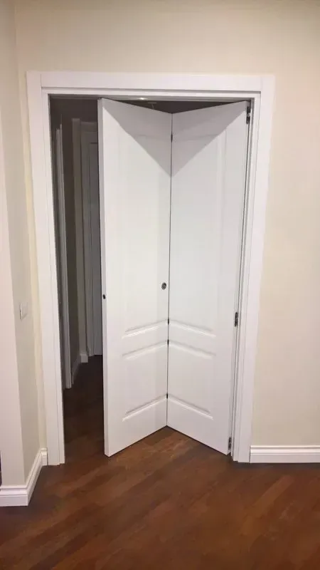 Una porta pieghevole bianca è aperta in una stanza con pavimenti in legno.