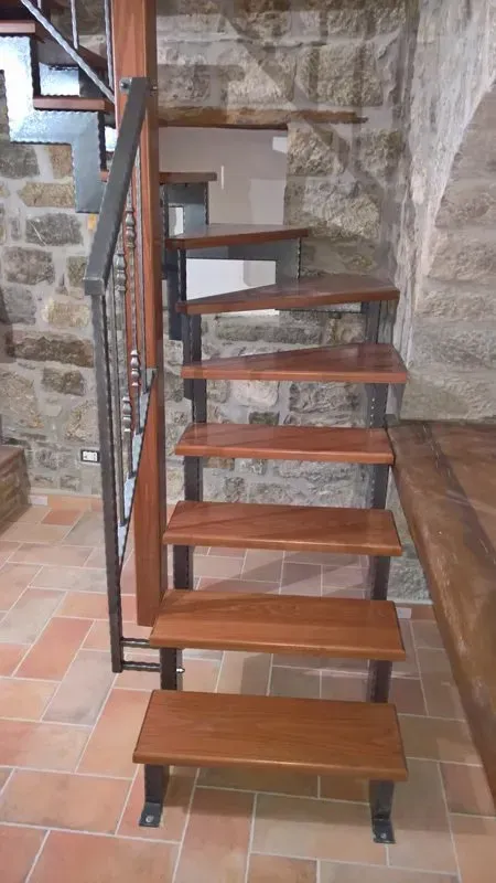 Una scala di legno con ringhiera di metallo in una stanza con un muro di pietra.