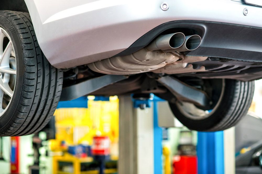 Underside of A Silver Car Lifted on A Blue Hydraulic Lift in A Repair Shop — Hervey Bay Brake and Exhaust in Pialba, QLD