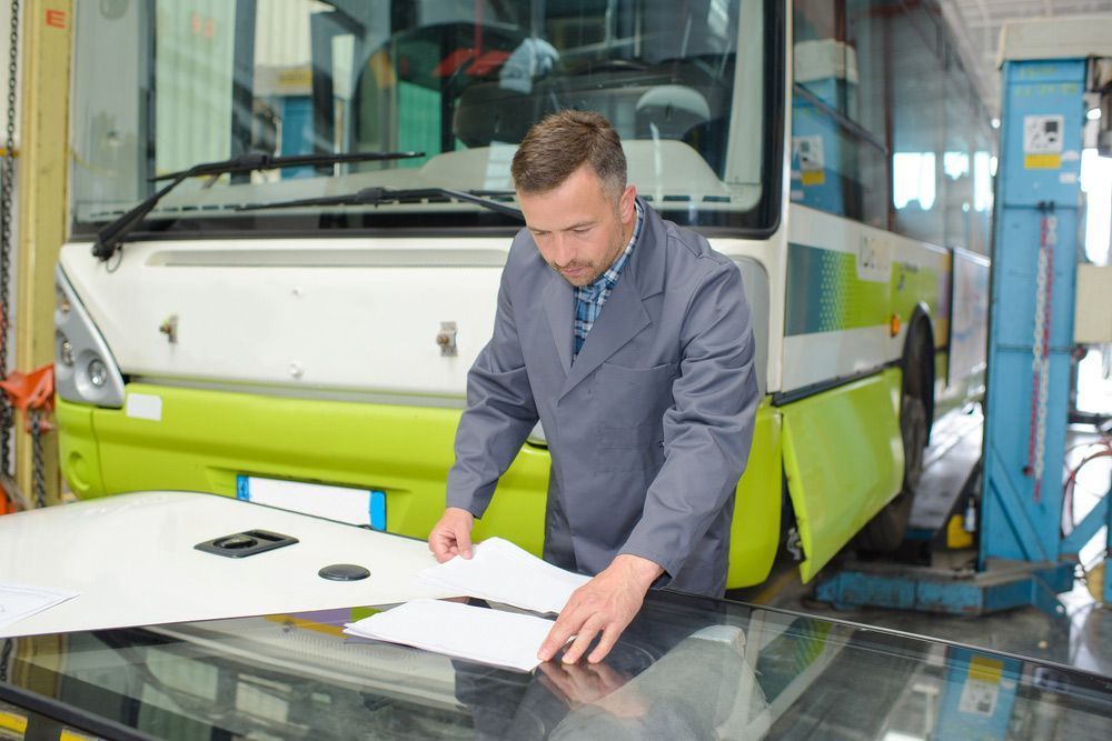 A Mechanic Inspects Paperwork in Front of A Bus in A Garage — Hervey Bay Brake and Exhaust Pialba, QLD