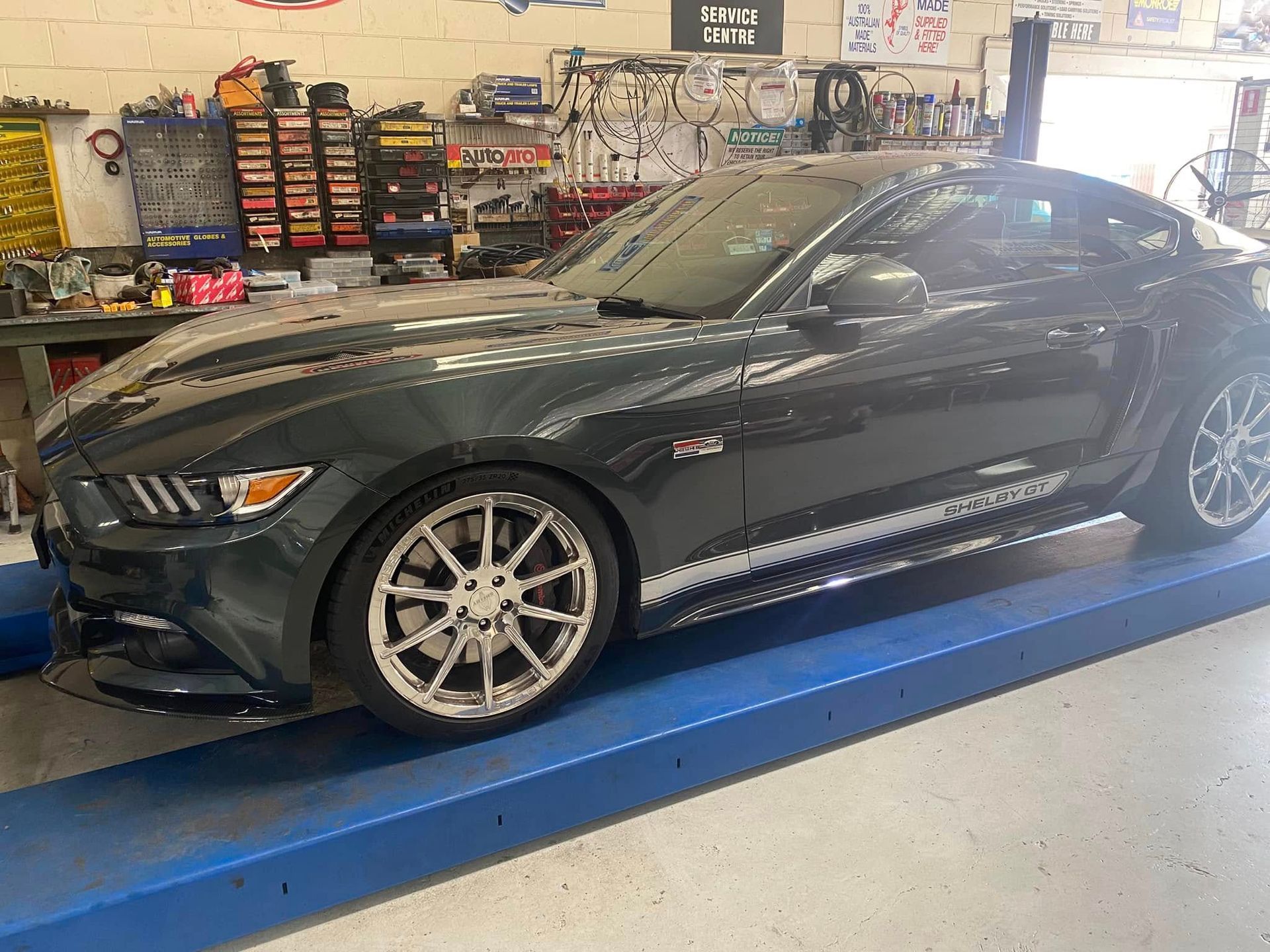 A Dark Gray Ford Mustang on A Blue Lift Inside a Cluttered Garage — Hervey Bay Brake and Exhaust in Pialba, QLD