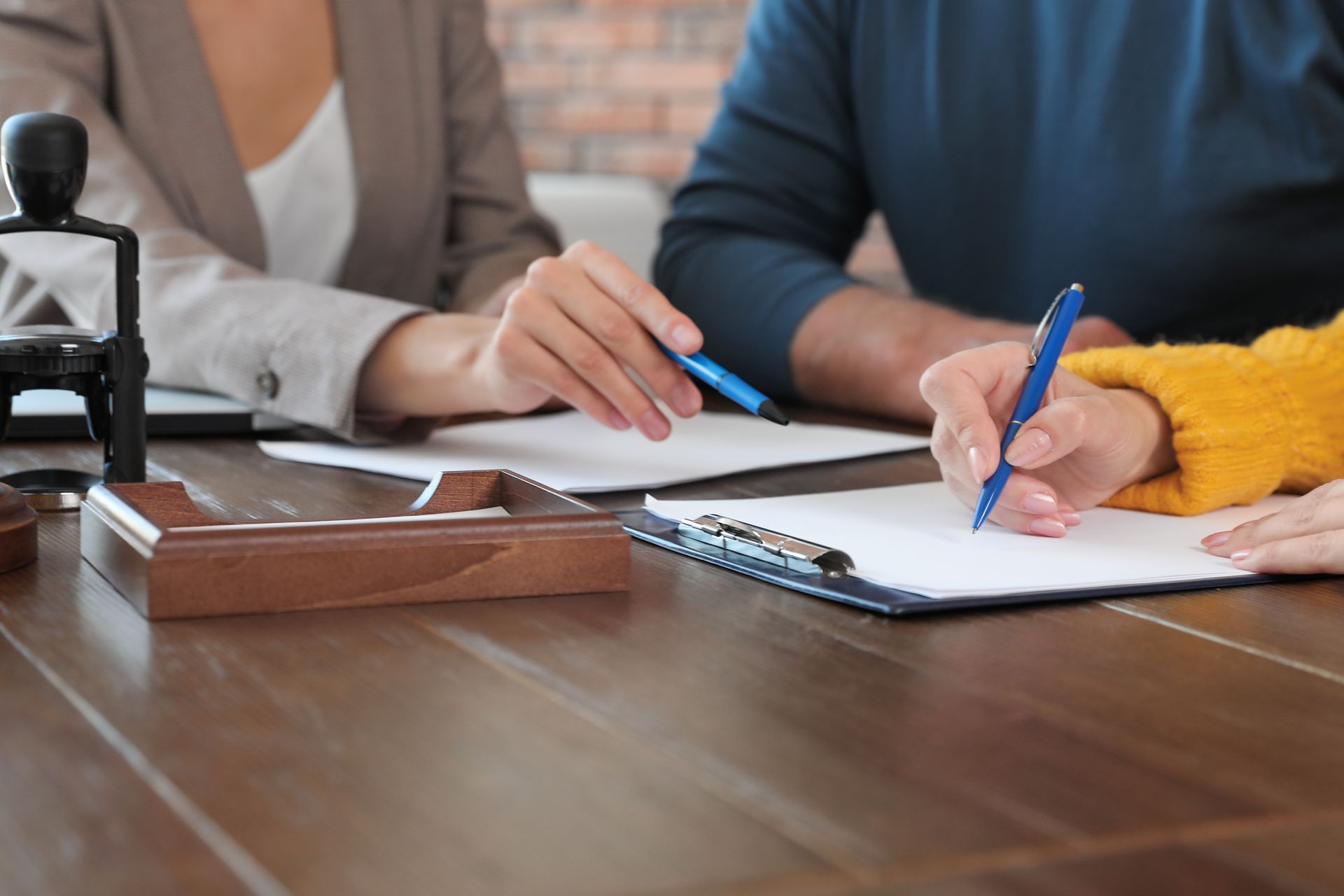 People signing documents at a table; a notary stamp is present.
