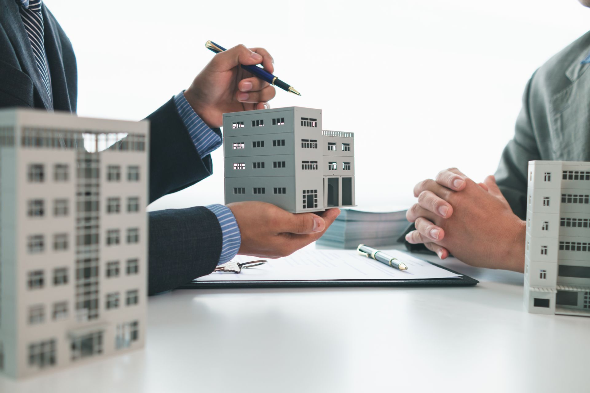 Person in a suit points at a model building while presenting to a seated person.