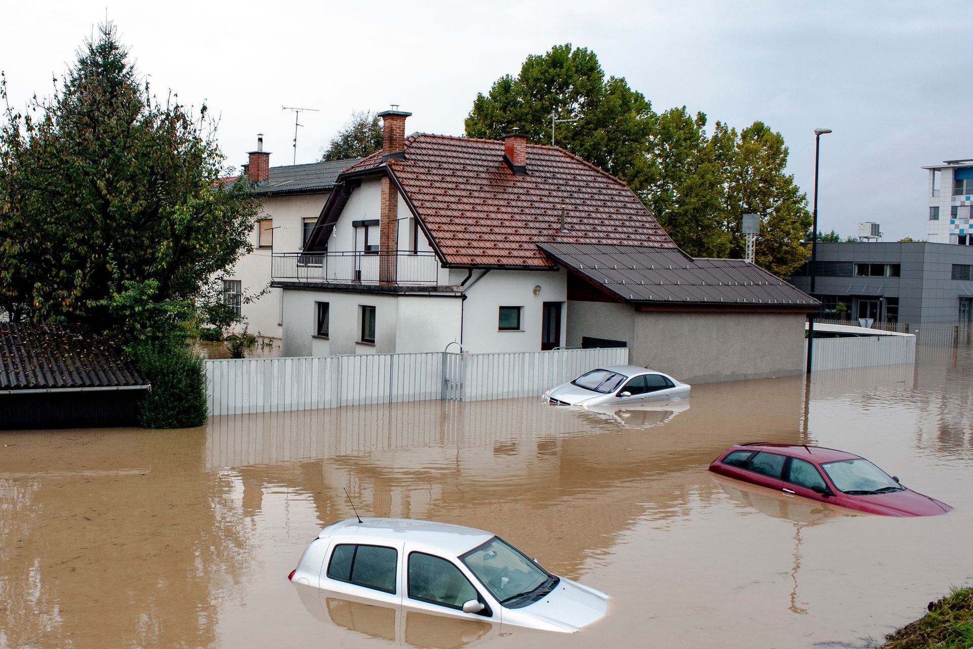 Flooded residential area; cars submerged in murky brown water near a house with an orange roof.