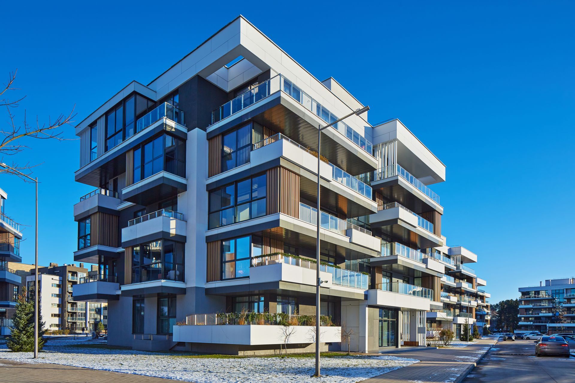 Modern multi-story apartment building with balconies, glass windows, and blue sky.