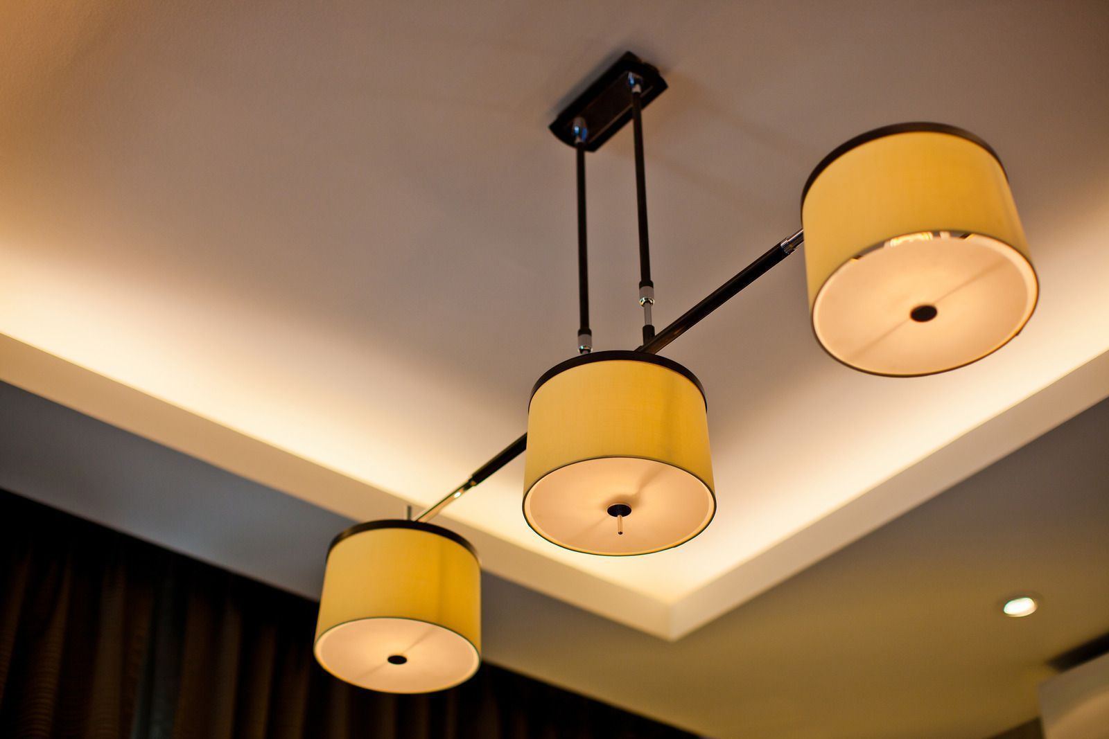 Three-light pendant lamp with cylindrical yellow shades hanging from a ceiling.
